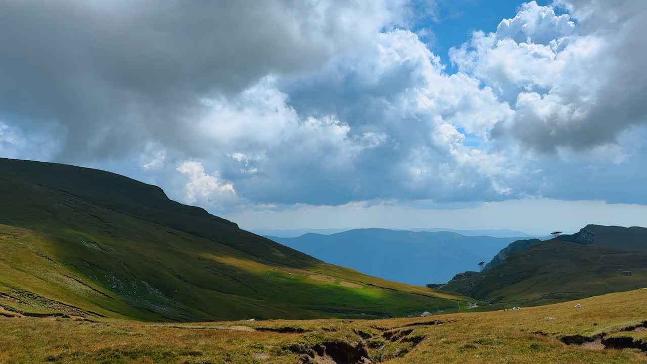 Vista su colline erbose sotto un cielo nuvoloso tra le montagne durante il giorno. Colline erbose si ergono su entrambi i lati con nuvole sopra, in un paesaggio montano durante il giorno.