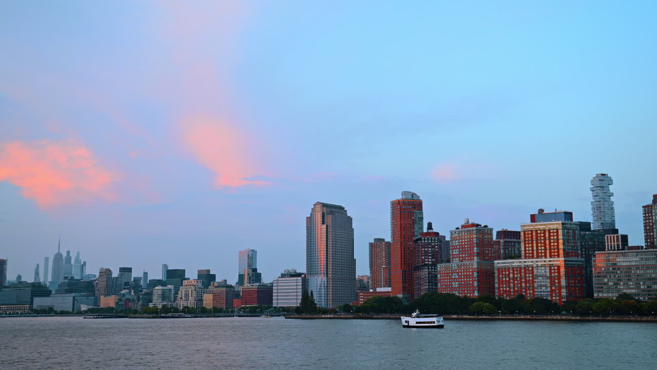 Udsigt på mellemafstand over Manhattans skyline under lyserøde skyer. Byskyline med forskellige skyskrabere under en stor himmel med levende lyserøde solnedgangsskyer.
