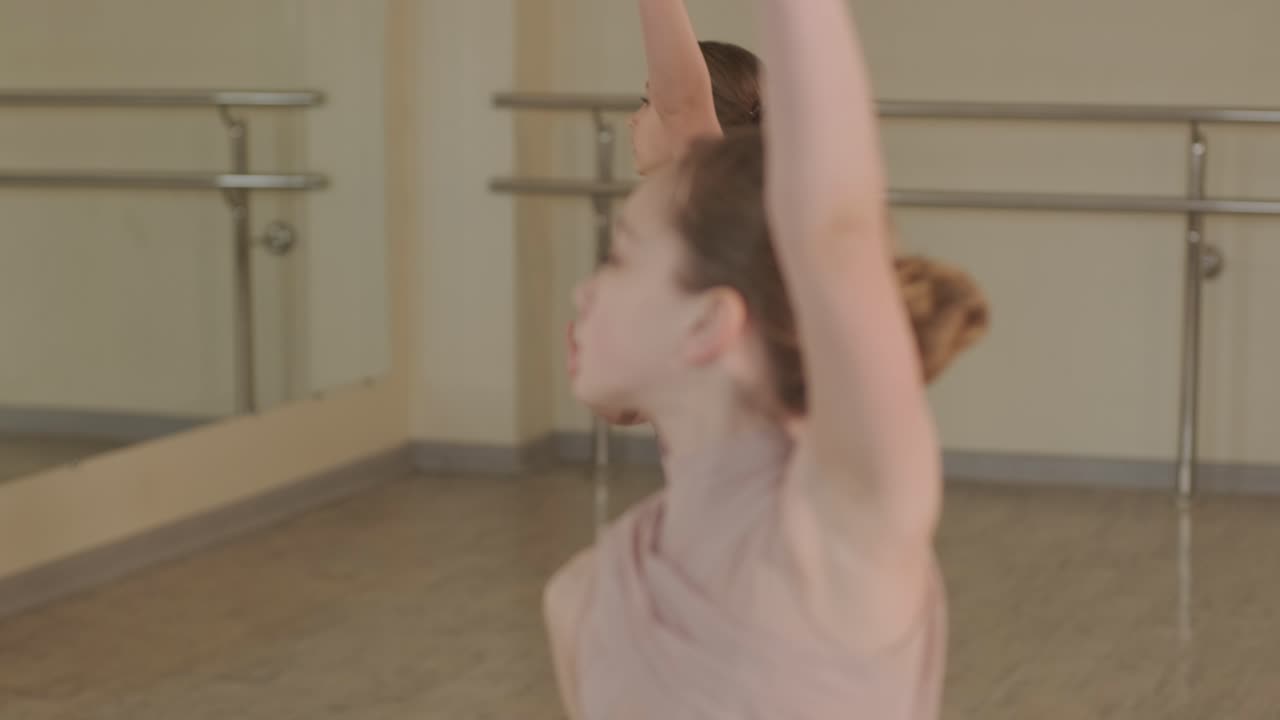 검은색 댄스웨어를 입은 젊은 발레 학생들이 나무 바닥과 벽에 장착된 바를 가진 넓은 발레 스튜디오에서 자세를 연습하는 그룹.