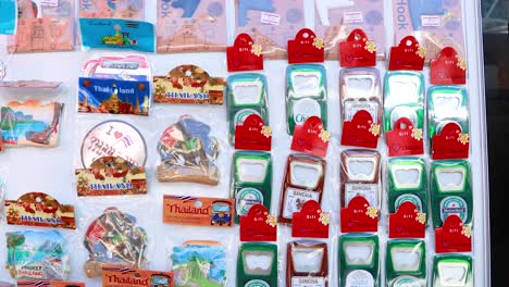 vibrant array of phuket-themed souvenirs on display. bright lighting highlights magnets, postcards, and keychains in a bustling market setting
