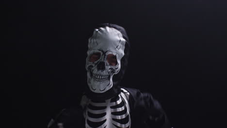fotografía de estudio de un niño vestido con un disfraz de esqueleto haciendo un truco o un regalo en halloween bailando contra un fondo negro