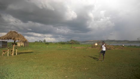 Toma-En-Cámara-Lenta-De-Un-Campo-De-Hierba-A-Orillas-Del-Lago-Victoria-Y-Un-Joven-Africano-Haciendo-Patadas