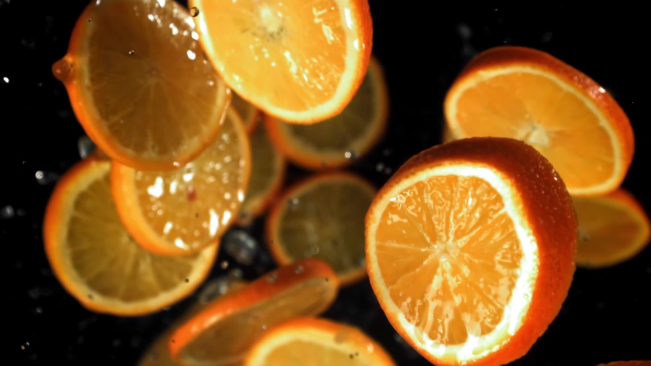 Fette d'arancia fresche che cadono al rallentatore con goccioline d'acqua