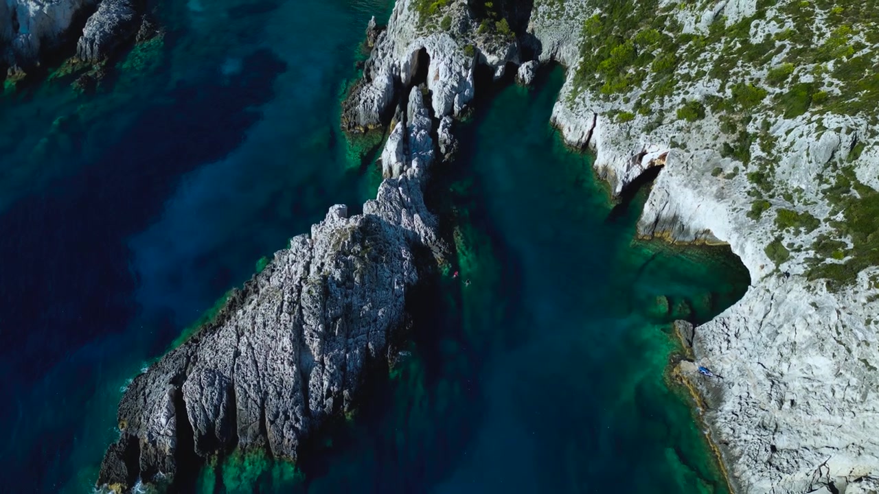 Ripresa aerea con drone di rocce calcaree frastagliate che incontrano il mare cristallino turchese in Grecia