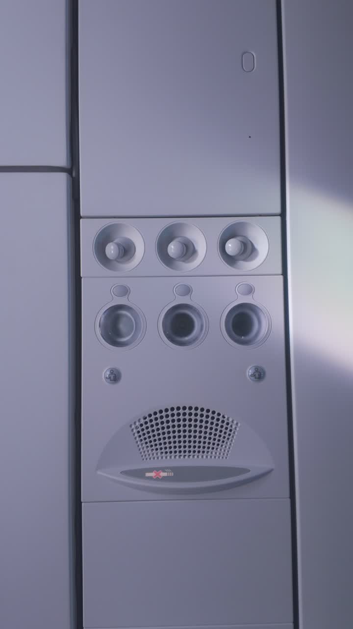 Airplane cabin Overhead panel with reading lights and air vents revealed by smooth tilt-down camera movement in airplane cabin, vertical video