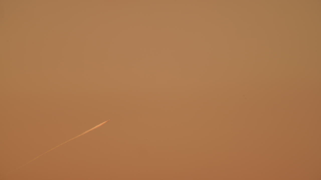 Jet airplane leaving a long white trail in the clear sky during sunset with warm orange gradient