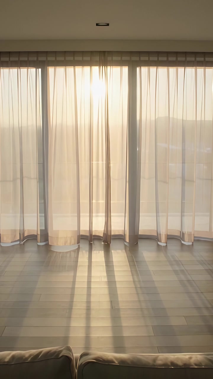 Vídeo vertical: Sol projetando sombras através de cortinas transparentes nas portas, movendo-se pelo chão e revelando um sofá.