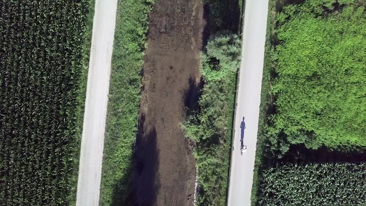 vista superior aérea sobre un ciclista que proyecta una larga sombra en el valle de sugana, italia con un dron volando hacia adelante