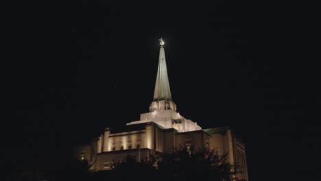 mormon church building at night with birds flying around spire and the angel moroni backlit by the moon | lds temple in gilbert, arizona