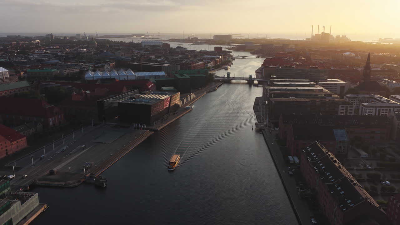 Aerial drone view of the Nyhavn canal and cityscape during golden hour, with boats and modern buildings along the waterfront in Copenhagen, Denmark