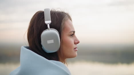 close-up side view of young woman walking while listening to music with headphones on, focusing on her surroundings, calm, peaceful walk in an outdoor environment with focus on her expression