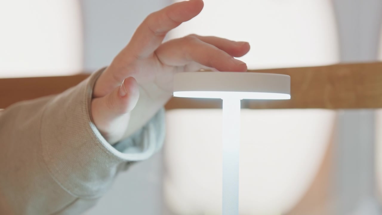 Close up of person hand interacting with top surface of illuminated white cylindrical object likely in soft indoor lighting. interaction involves gentle touch and movement near or on glowing