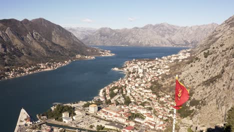 AERIAL---Bay-of-Kotor-and-national-flag-on-a-beautiful-sunny-day,-Kotor,-Montenegro