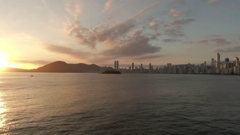 Vuele-Sobre-El-Paisaje-Marino-En-La-Ciudad-De-La-Playa-De-Balneário-Camboriú-Con-La-Isla-De-Las-Cabras-Durante-La-Puesta-De-Sol-En-Brasil