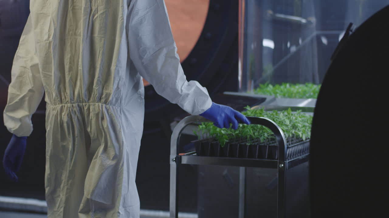 Scientist in Protective Gear Tending to Plants in a Controlled Environment