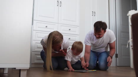 a family of three in white t-shirts and blue jeans sitting on the floor of their bedroom playing with the boy in intellectual games. slow-motion shooting happy family