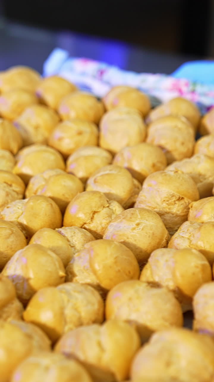 Brown baked balls of future desserts being pulled out of oven. Big baking sheet covered with profitroles. Confectionary concept. Vertical video