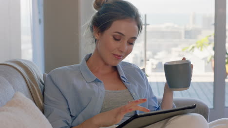 hermosa mujer joven usando una tableta digital relajándose en el sofá en casa navegando en línea bebiendo café disfrutando de un estilo de vida cómodo
