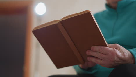 lonely pensioner in green teal sweater holding brown book with one hand, deeply focused on reading, soft indoor lighting, tranquil atmosphere, quiet personal moment of reflection