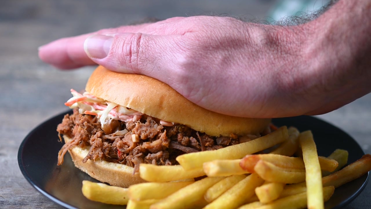 Mano che schiaccia un sandwich di pulled pork con patatine fritte