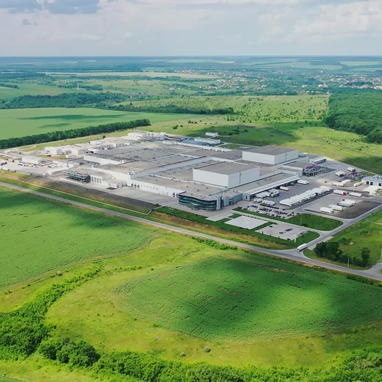 Industry surrounded by green nature. View from above on modern manufacture on field in a bright summer day. Aerial view.