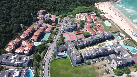 aerial drone shot of a beautiful turquoise blue sea beach with mountains covered in vegetation near the coast with many summer condominiums amid the atlantic forest and ocean in florianopolis