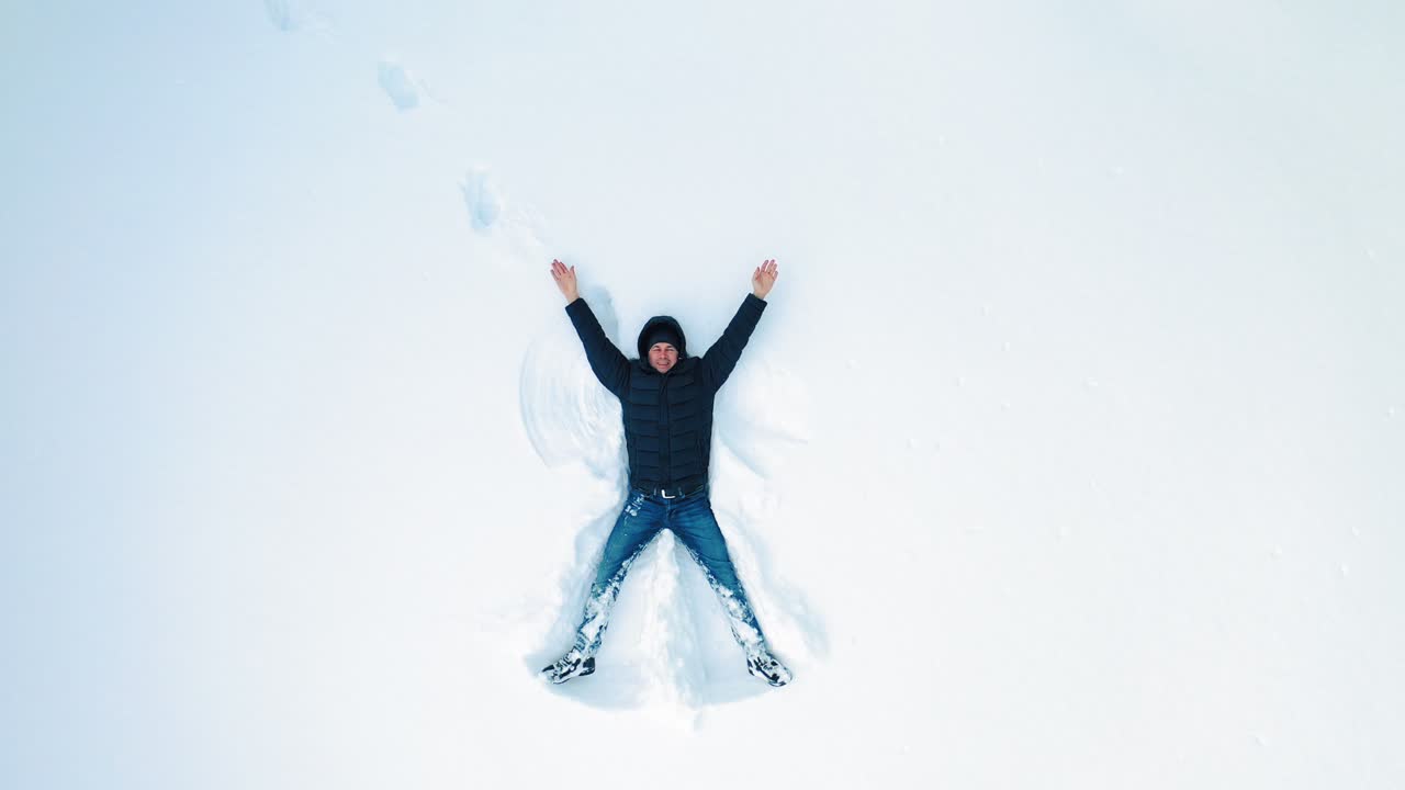 Man lying on snow in winter holiday. Aerial view of snow angel made by man in the snow