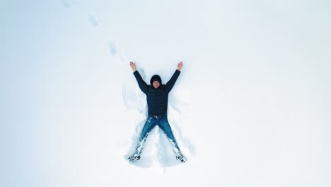 man lying on snow in winter holiday. aerial view of snow angel made by man in the snow