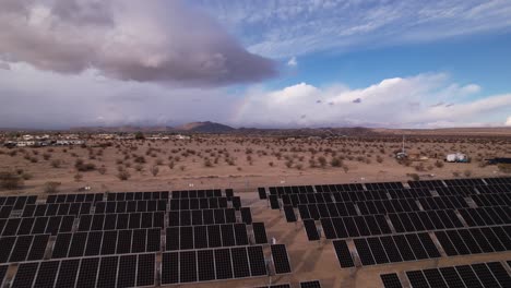 aerial drone footage of solar panel field in joshua tree national park on a sunny day with rainbow in the background, reveal moving backwards