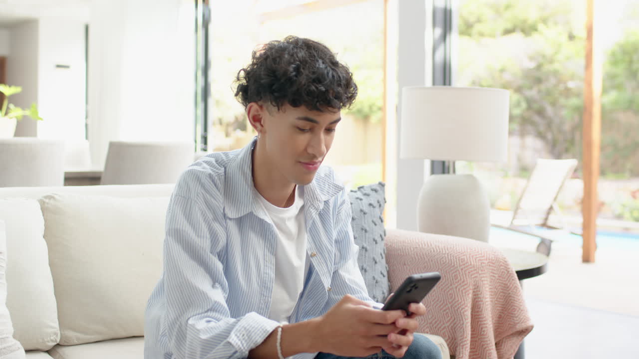 Sitting on couch, teenage boy holding smartphone and smiling at home