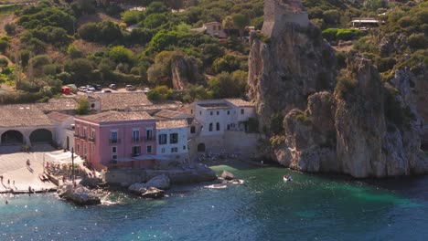 Aerial drone shot panning right close-up over a resort and private beach featuring huge rocks at Tonnara di Scopello, Sicily, Italy, highlighting the natural beauty of the coastline during summer