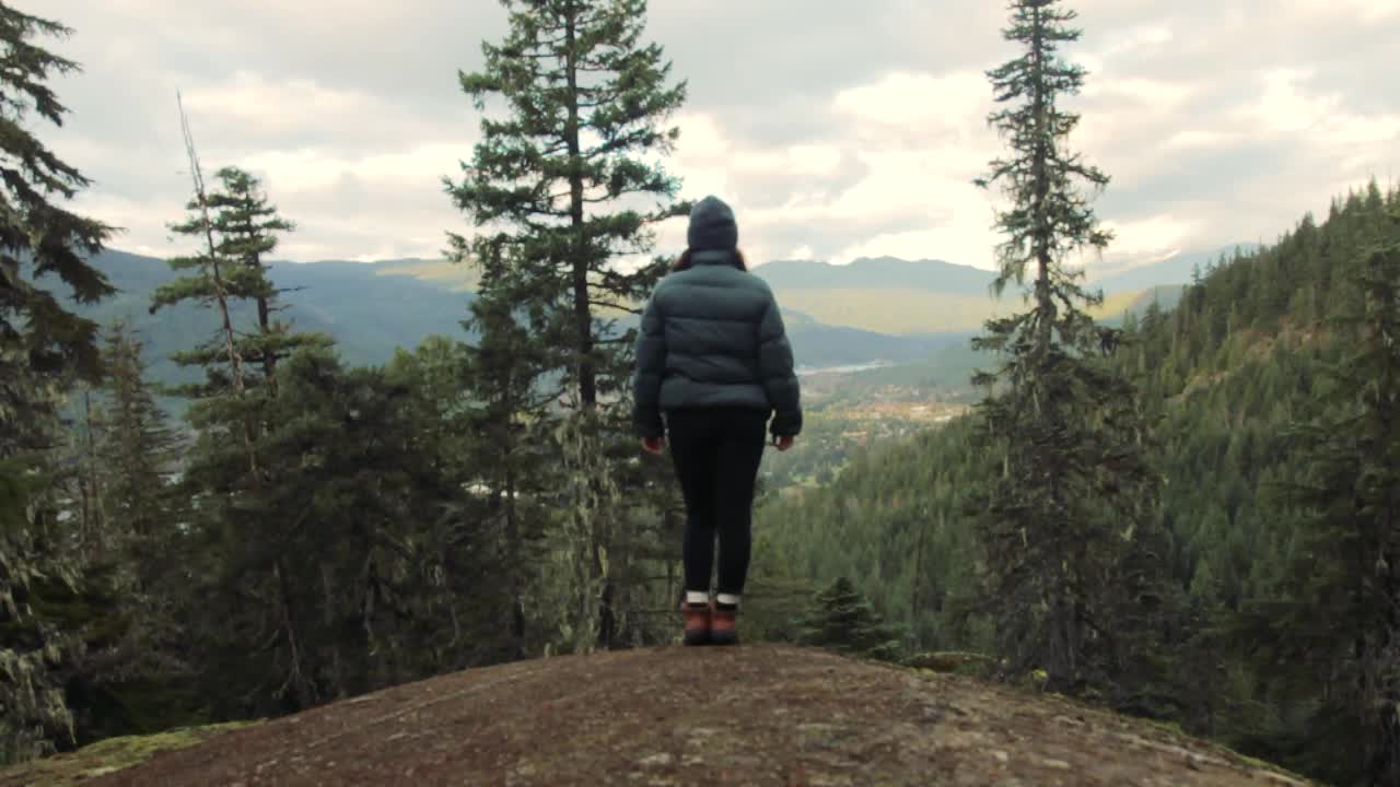 Beautiful young adult female reaches top of the hill to admire the view of Whistler BC