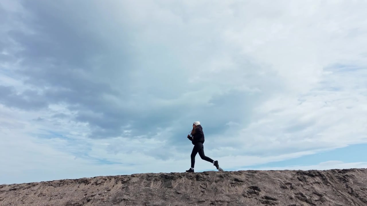 Woman Running on Sandy Dune Against Cloudy Sky