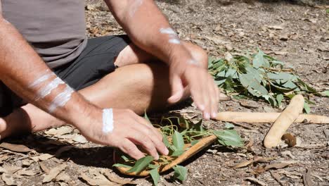 Australian-Aboriginal-Smoking-Ceremony,-man-preparing-green-leaves-on-a-traditional-wooden-bowl-as-part-of-an-ancient-indigenous-custom