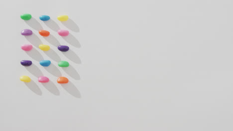 video of overhead view of rows of multi coloured sweets with copy space over white background