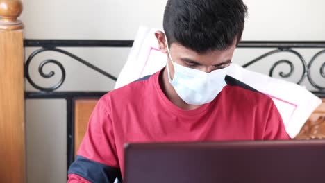 joven con una máscara estudiando en una computadora portátil en casa