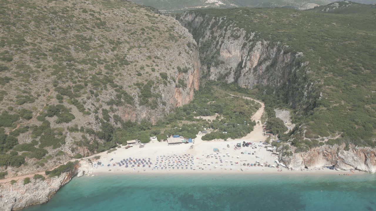 드론 촬영 gjipe 해변 알바니아 해변에 관광객과 산과 바다 근처의  ⁇ 은 파란 물  ⁇ 빛과 밝은 날과 녹색 자연 주변에 태양 침대 수건 로그