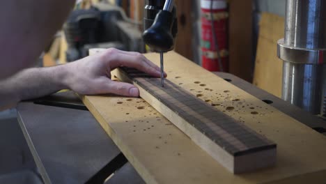 luthier's hands drilling holes in fretboard for fretmarkers with drill press machine