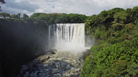 Aerial-drone-forwarding-shot-of-featuring-a-waterfall-going-through-a-Mexican-forest-with-lush-green-vegetation-on-a-sunny-day