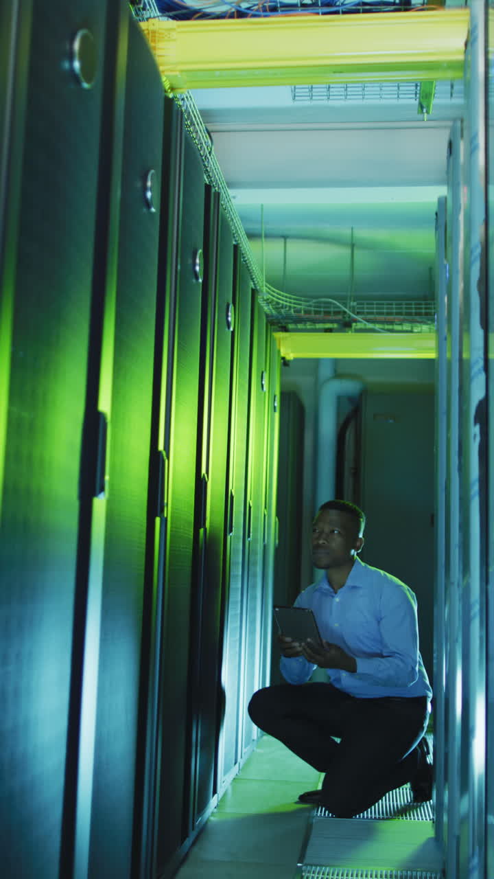 disparo vertical de un hombre afroamericano arrodillado cerca de un servidor en una sala de servidores