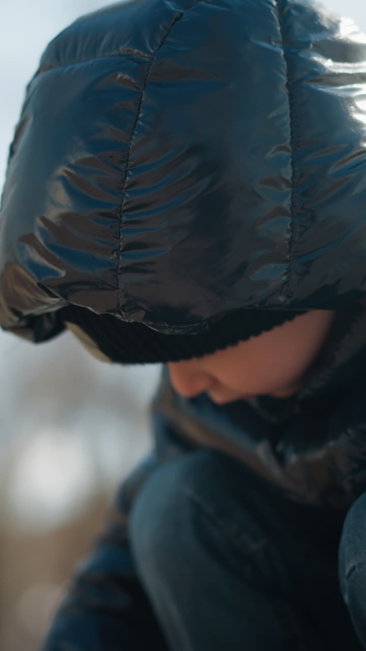 반이는 검은색 재, 헤드 워머, 청바지를 입고, 나무의 흐릿한 배경과 함께 그의 활동에 깊이 집중 한 어린 소년