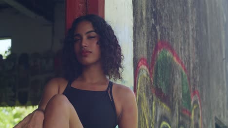 young woman with curly hair posing in front of graffiti wall