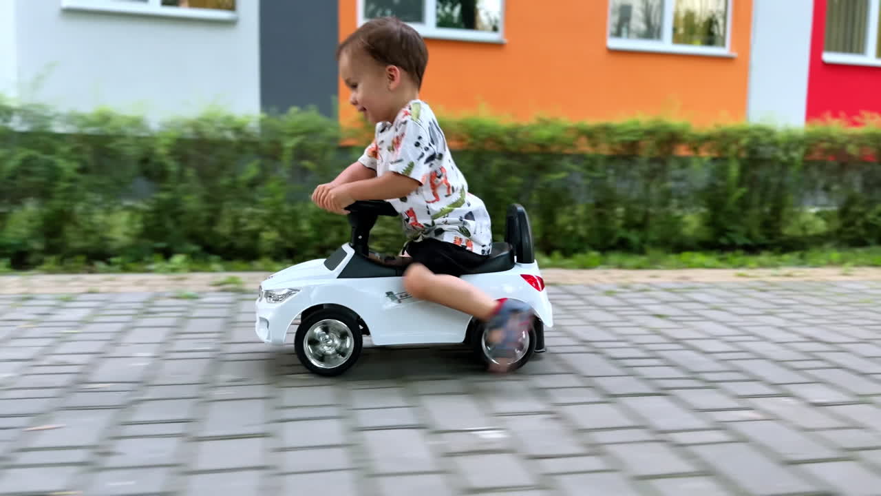 Beautiful baby boy riding quickly a toy car. Happy healthy kid having fun outdoors in summer.