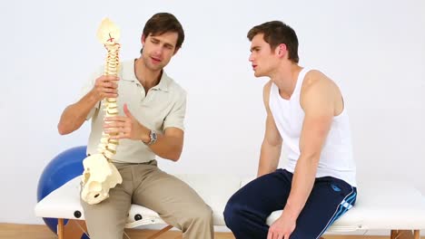 physiotherapist speaking to patient showing him a spine model