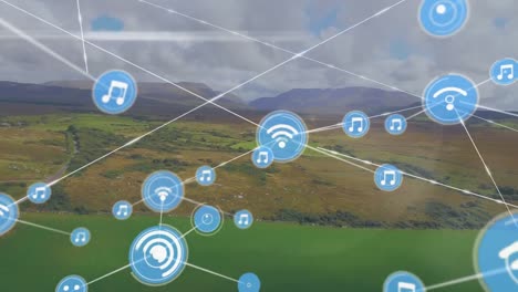 Animation-of-icons-connected-with-lines,-aerial-view-of-green-field-against-mountain-and-cloudy-sky