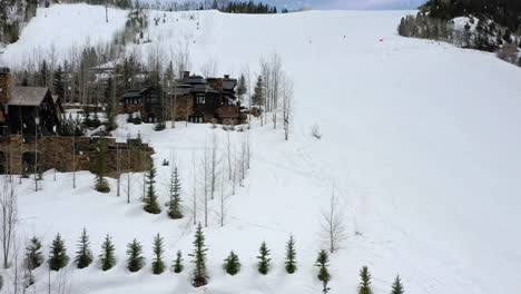 Modern-slopeside-winter-homes-during-snowfall,-aerial-drone-fly-over-view