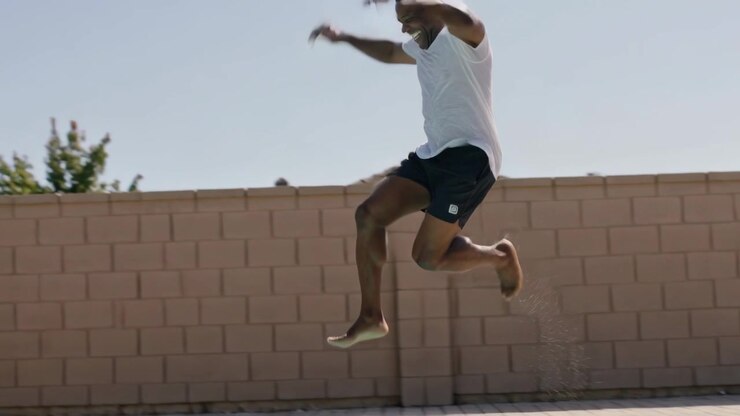 Running man wearing white tee and dark shorts training, launching off pool deck into water, splash