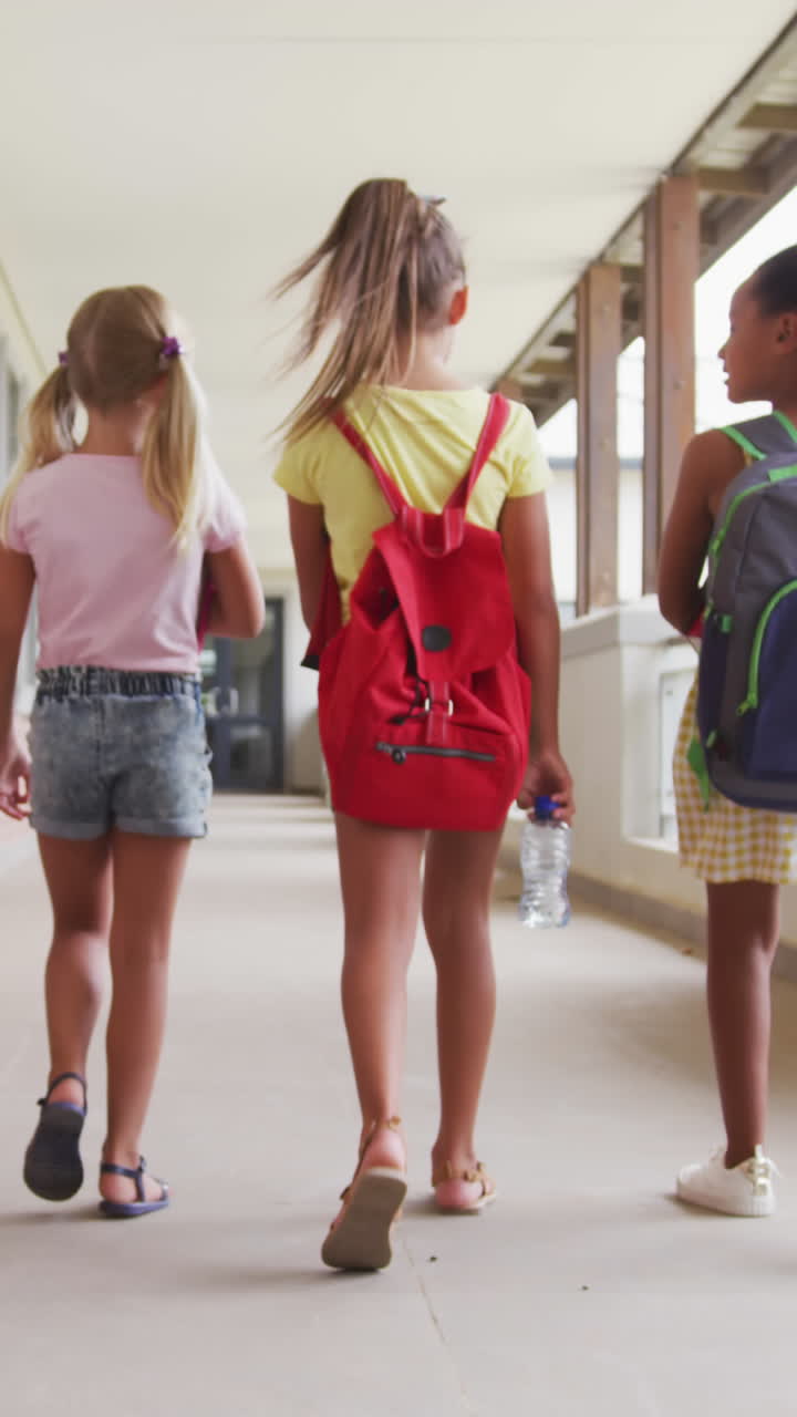 video de vista trasera de niñas diversas caminando en el pasillo de la escuela y hablando