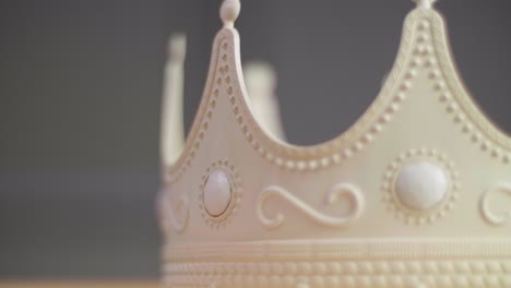 close up of a beige crown spinning on a pedestal with ornaments and white pearl jewels with peaks jagged out of plastic. with a neutral grey background. shot in 4k.