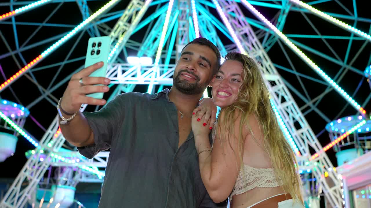 Couple taking a selfie at a Ferris wheel at night